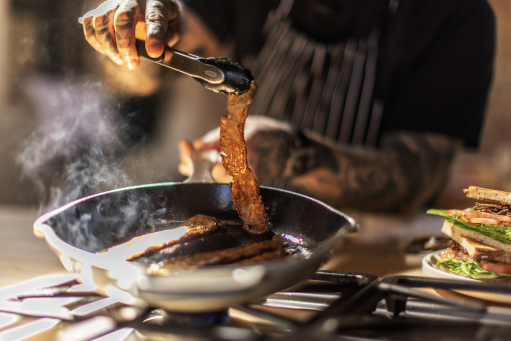 person-with-apron-grilling-protein-on-pan