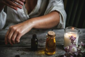 person-applying-essential-oil-on-arm-with-dropper-on-table-with-candle
