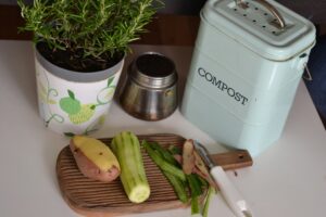 small-cutting-board-with-peeled-vegetables-beside-potted-plant-and-compost-machine