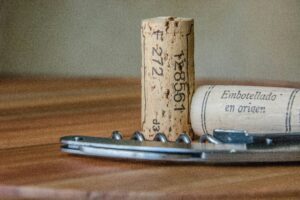 cork-standing-on-wood-table-with-wine-opener-and-another-cork-lying-down