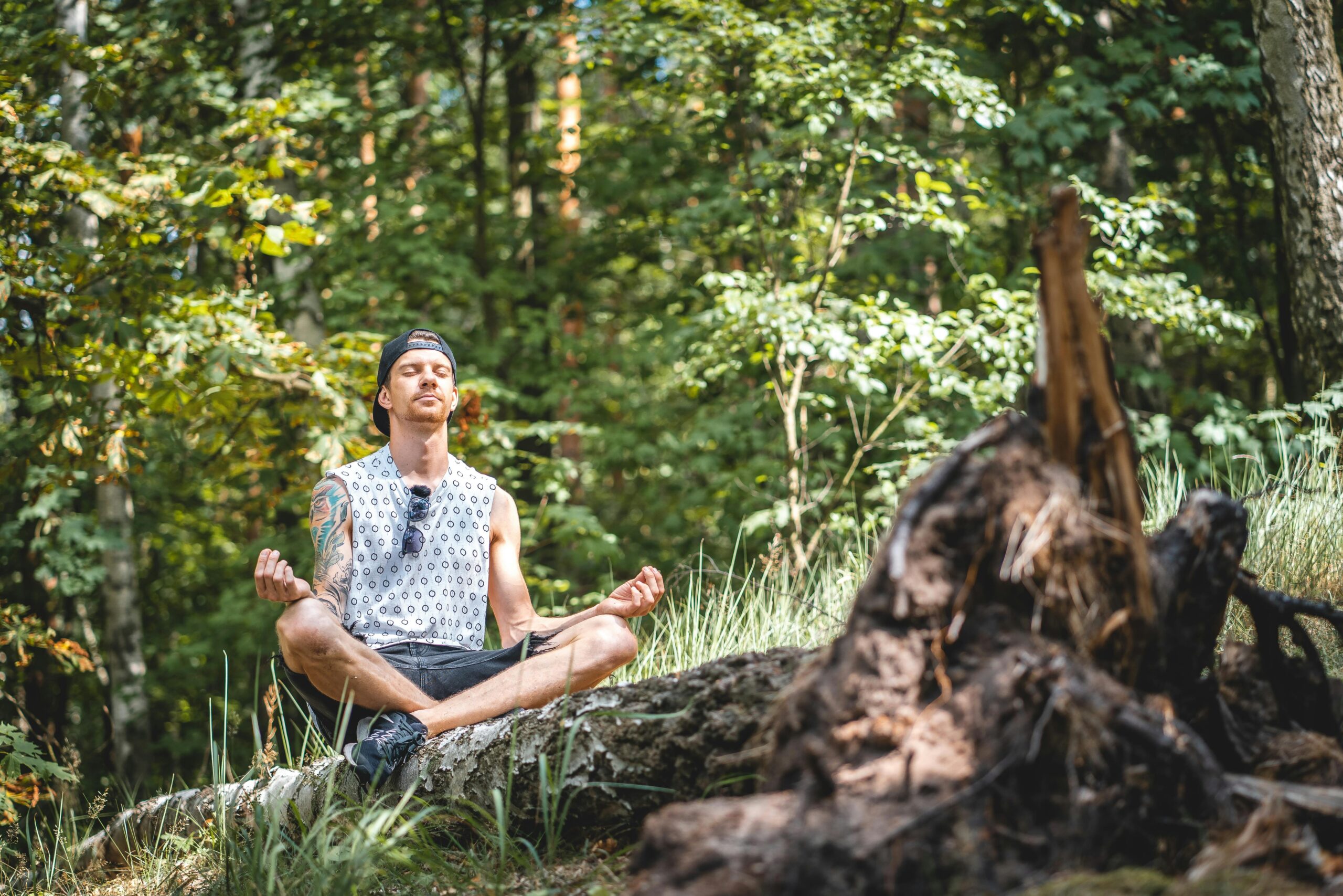 man-with-cap-meditating-beside-rock-formation-in-forest