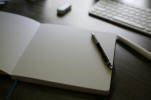 open-notebook-with-mechanical-pencil-and-keyboard-in-background