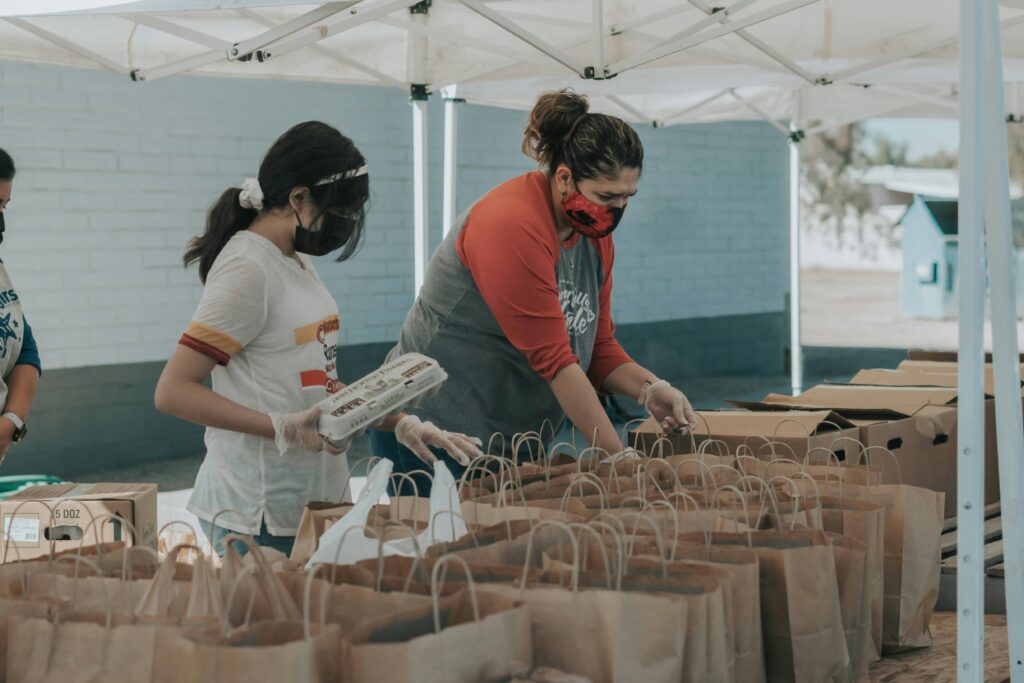 two volunteers packing food into paper bags