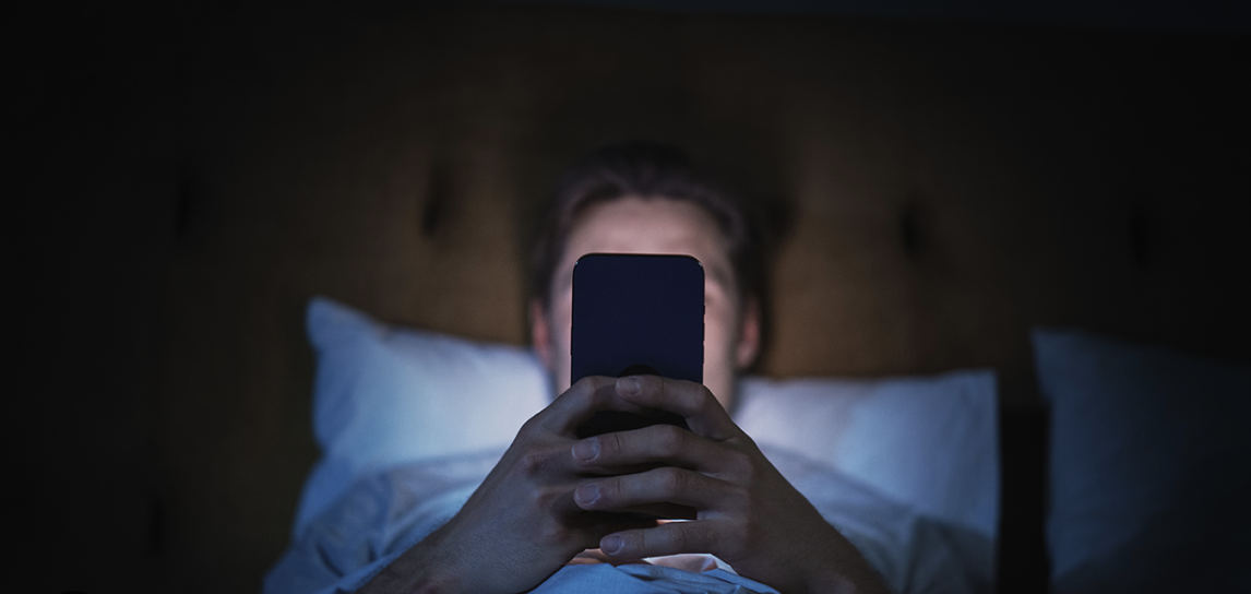 person watching phone in dark room in bed