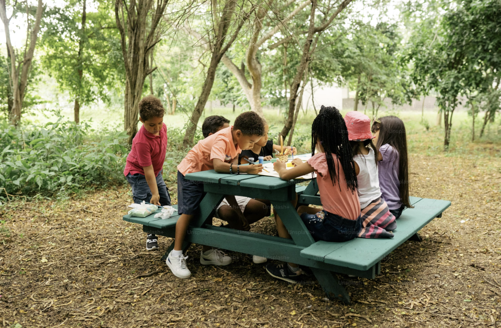 children sitting at picnic table among the trees on a sunny day