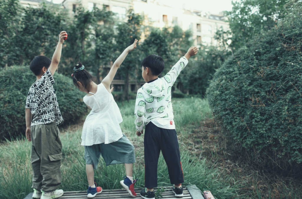 three kids striking poses in grass surrounded by greenery
