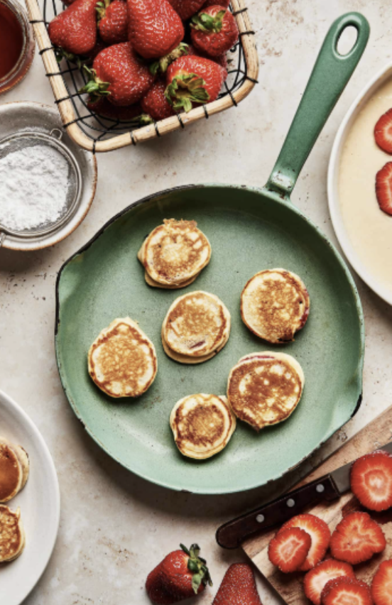 mini pancakes on green pan surrounded by strawberries
