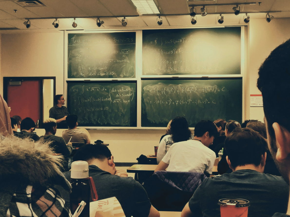students sitting in classroom with teacher at whiteboard teaching