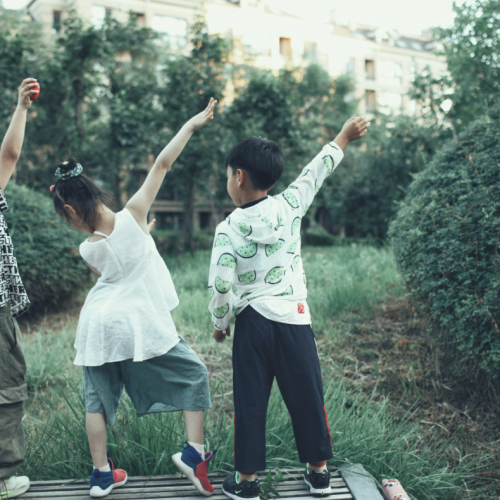 three kids striking poses in grass surrounded by greenery