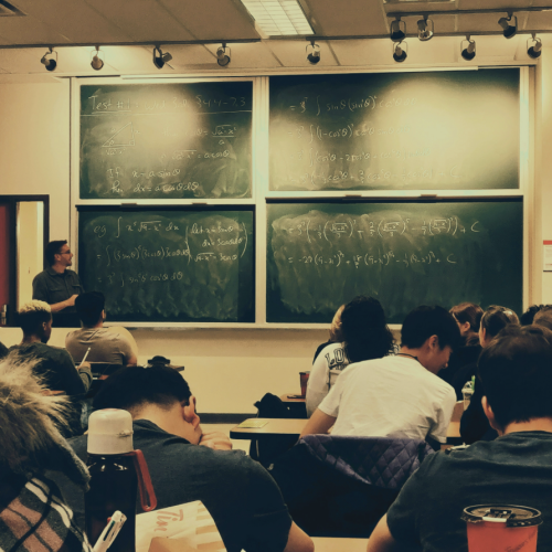 students sitting in classroom with teacher at whiteboard teaching